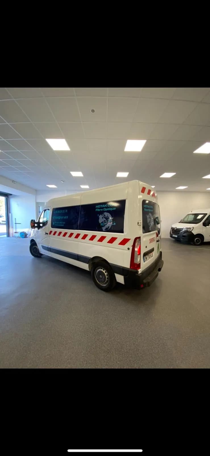 Utilitaire blanc avec visuels adhésifs sur les vitres arrière et bandes réfléchissantes rouges, en atelier