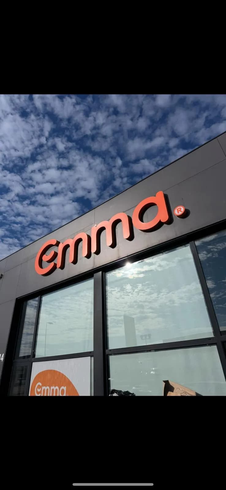 Enseigne en lettres relief orange posée sur une façade sombre, au-dessus de la vitrine