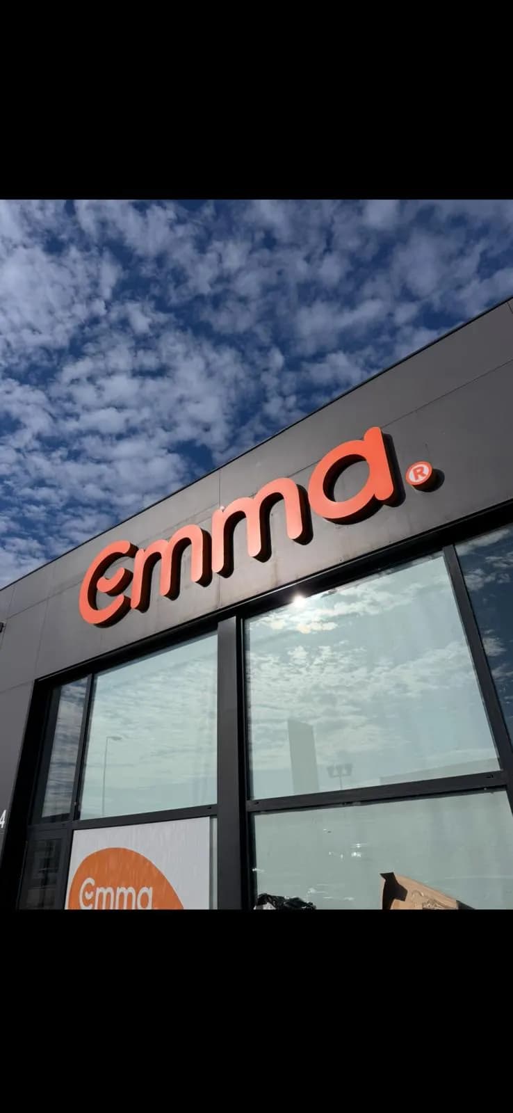 Lettres relief orange d'une enseigne de façade vues en contre-plongée sur ciel bleu